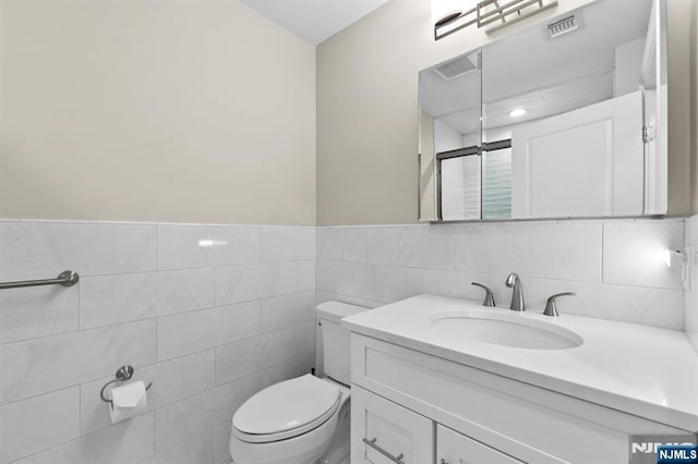 bathroom featuring tile walls, visible vents, toilet, a shower stall, and vanity