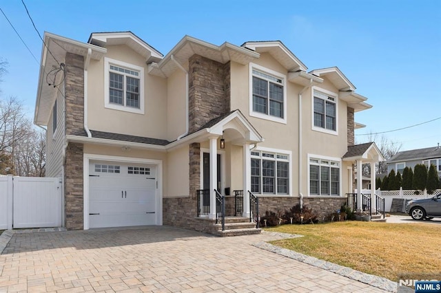 view of front of property with stone siding, fence, decorative driveway, and stucco siding