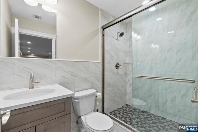 full bath featuring visible vents, toilet, vanity, a shower stall, and tile walls