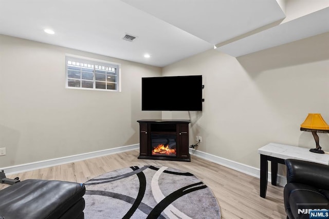 living area with baseboards, visible vents, wood finished floors, and a glass covered fireplace