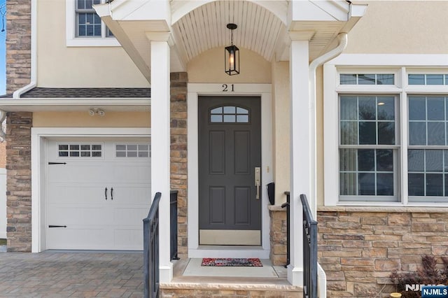 property entrance featuring a garage, stone siding, decorative driveway, and stucco siding