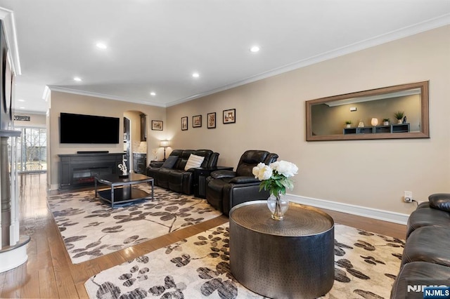 living area featuring arched walkways, hardwood / wood-style flooring, baseboards, a glass covered fireplace, and crown molding