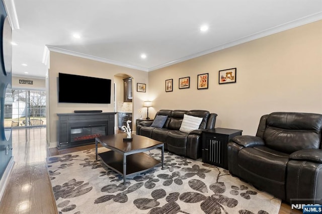 living area featuring arched walkways, a glass covered fireplace, wood finished floors, and crown molding