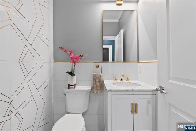 half bathroom featuring crown molding, tile walls, toilet, wainscoting, and vanity