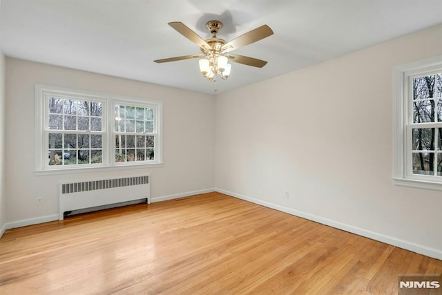 unfurnished room featuring a ceiling fan, light wood-type flooring, radiator, and baseboards