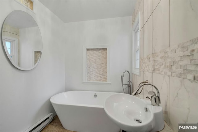 bathroom featuring a freestanding tub, a baseboard radiator, a sink, and tile walls