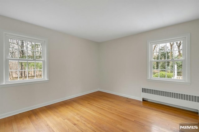 empty room featuring baseboards, light wood finished floors, and radiator heating unit