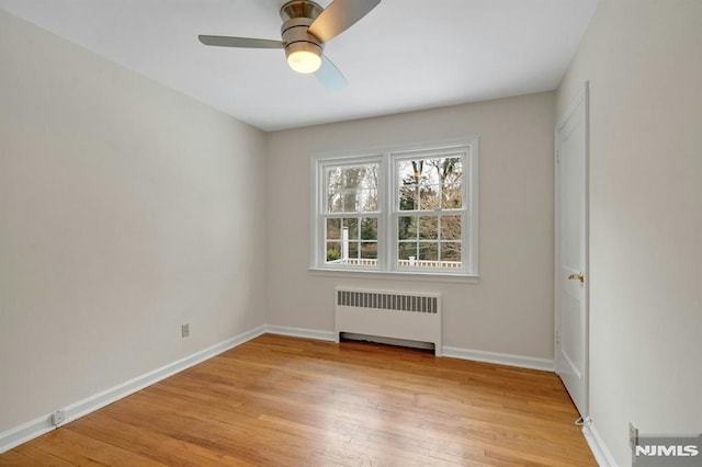 spare room featuring baseboards, ceiling fan, light wood-style flooring, and radiator