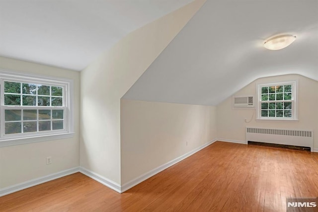 additional living space featuring vaulted ceiling, baseboards, wood finished floors, and radiator