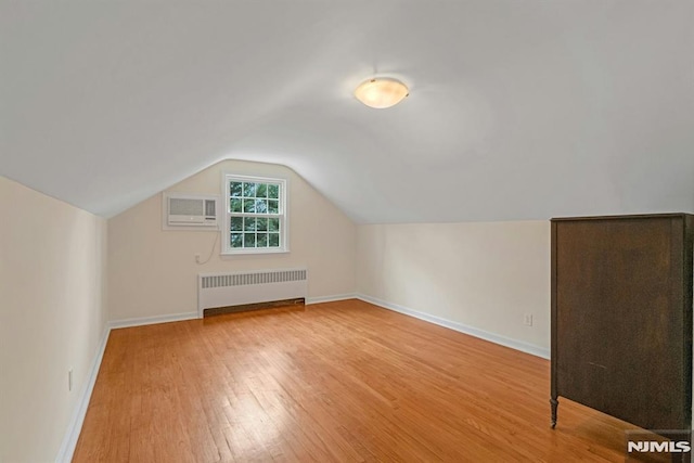 bonus room with radiator, vaulted ceiling, wood finished floors, a wall mounted air conditioner, and baseboards