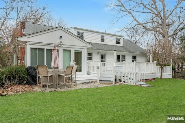 back of house with a deck, a yard, roof with shingles, and a chimney