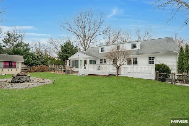 rear view of property with roof with shingles, a lawn, fence, a deck, and a fire pit