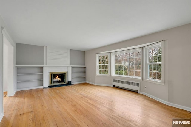 unfurnished living room with a large fireplace, radiator heating unit, light wood-style flooring, and a wealth of natural light