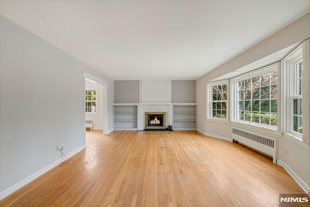 unfurnished living room featuring baseboards, radiator heating unit, a fireplace, and light wood-style floors