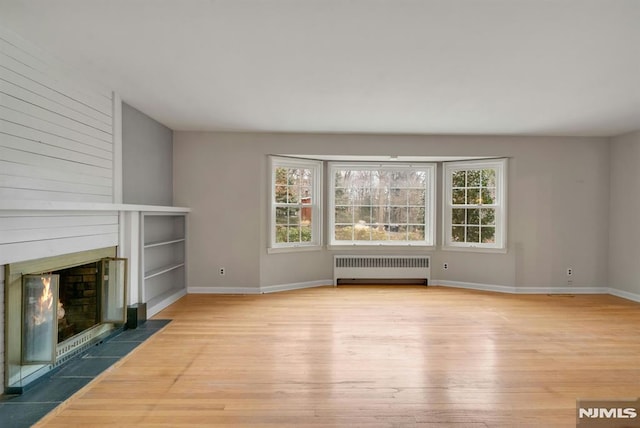 unfurnished living room featuring a large fireplace, radiator heating unit, wood finished floors, and a wealth of natural light