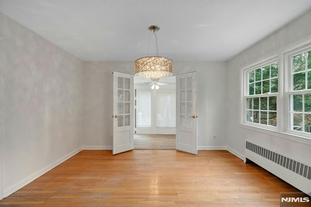 unfurnished dining area with light wood-style floors, radiator heating unit, baseboards, and french doors