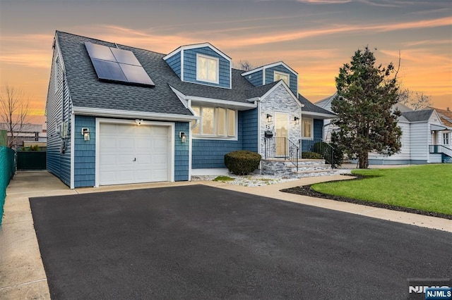 view of front facade with an attached garage, solar panels, a shingled roof, driveway, and a yard