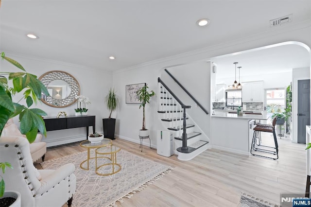 living area with light wood finished floors, a baseboard radiator, visible vents, stairway, and ornamental molding