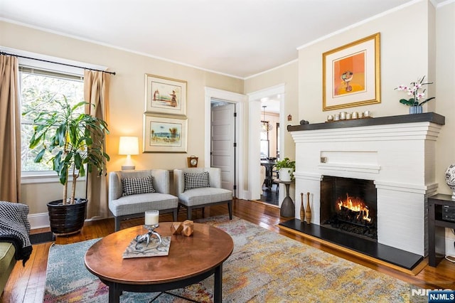 living area featuring a warm lit fireplace, hardwood / wood-style floors, baseboards, and crown molding