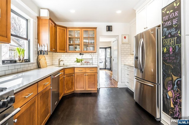 kitchen with stainless steel appliances, dark wood-type flooring, a sink, decorative backsplash, and glass insert cabinets