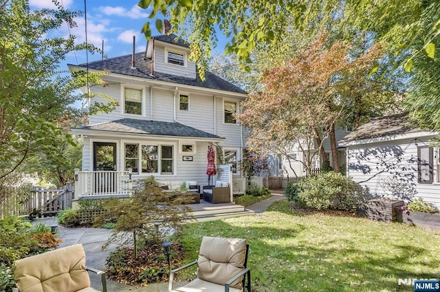 traditional style home featuring a front yard, roof with shingles, fence, and an outdoor living space