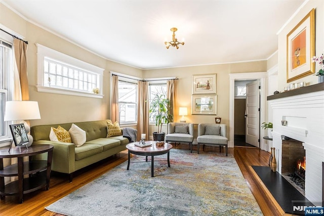 living area featuring a brick fireplace, crown molding, wood finished floors, and an inviting chandelier