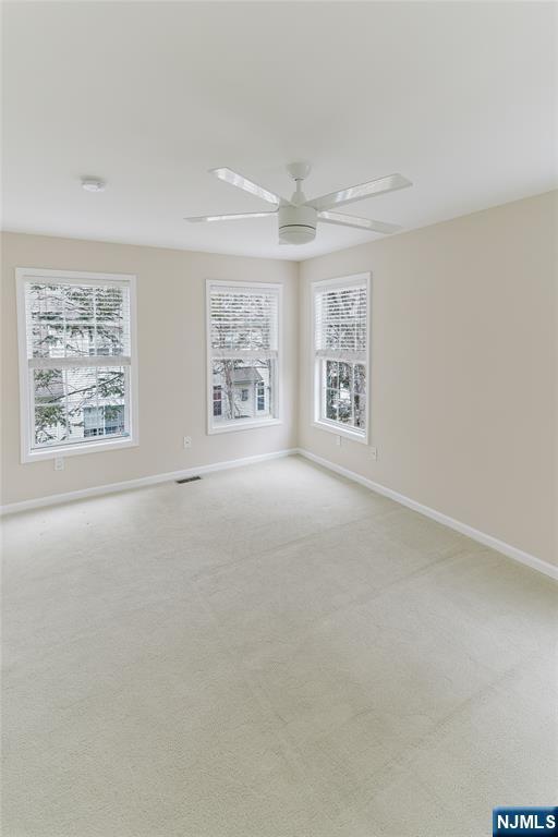 carpeted spare room featuring ceiling fan, visible vents, and baseboards