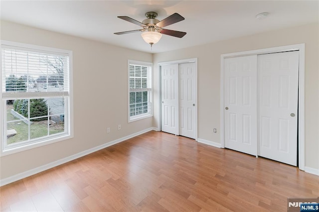 unfurnished bedroom with light wood-style floors, ceiling fan, baseboards, and two closets