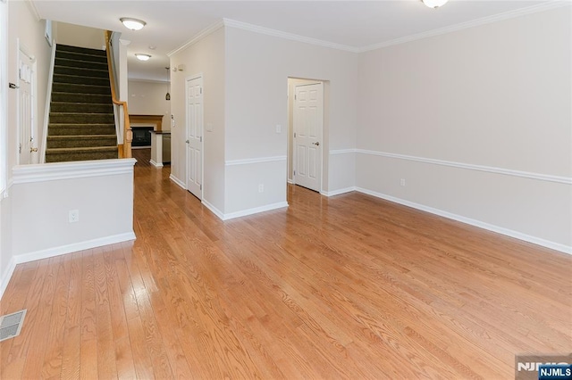 empty room featuring a fireplace, visible vents, baseboards, ornamental molding, and light wood-type flooring