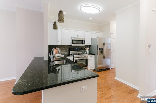 kitchen with white cabinets, appliances with stainless steel finishes, a peninsula, a sink, and backsplash