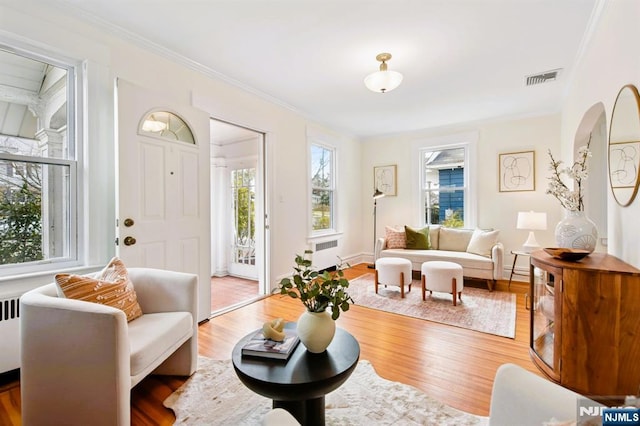 living area with radiator, wood finished floors, visible vents, and ornamental molding