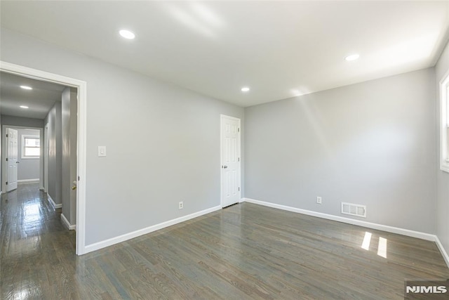 empty room featuring dark wood-style floors, baseboards, visible vents, and recessed lighting