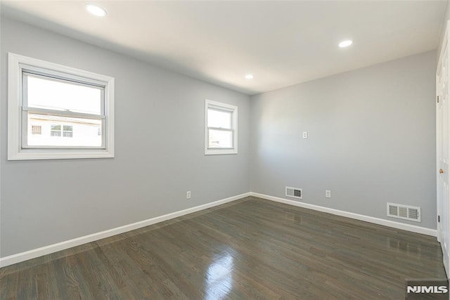 unfurnished room featuring baseboards, visible vents, and dark wood finished floors