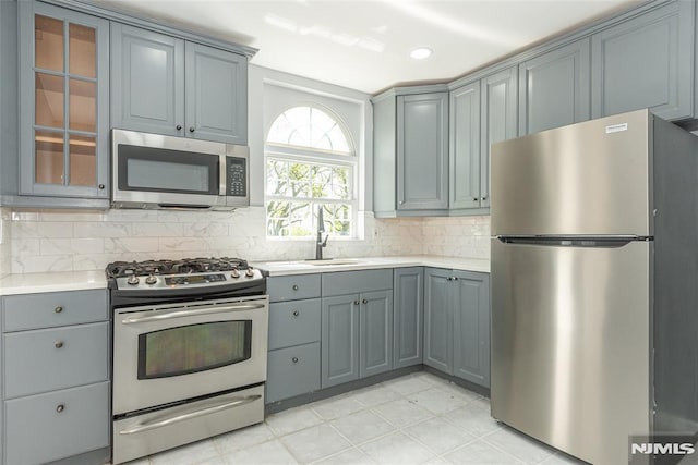 kitchen with appliances with stainless steel finishes, gray cabinets, light countertops, and tasteful backsplash