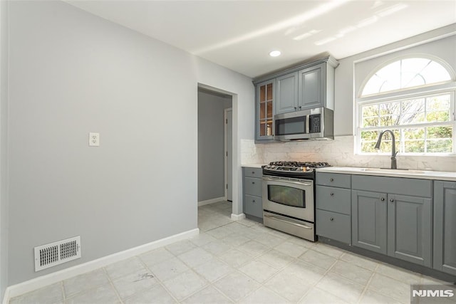 kitchen featuring stainless steel appliances, visible vents, backsplash, gray cabinetry, and a sink