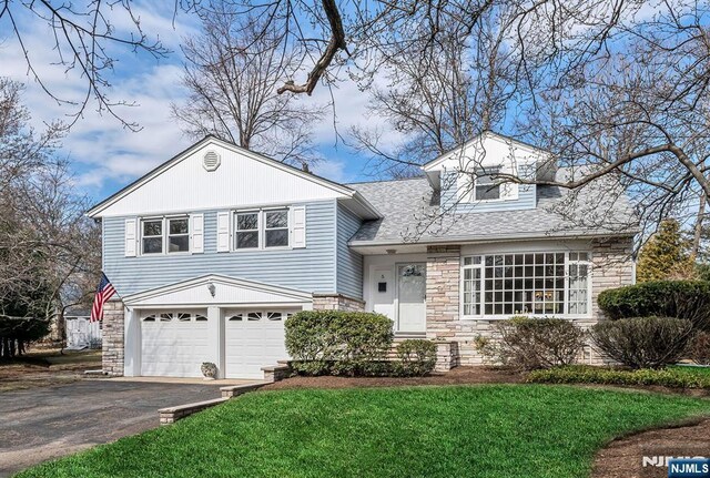 tri-level home with a front lawn, aphalt driveway, roof with shingles, a garage, and stone siding