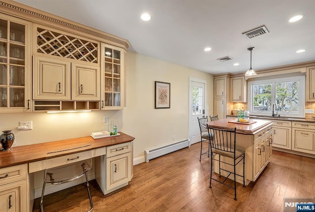 kitchen with visible vents, cream cabinetry, butcher block countertops, a baseboard heating unit, and built in desk