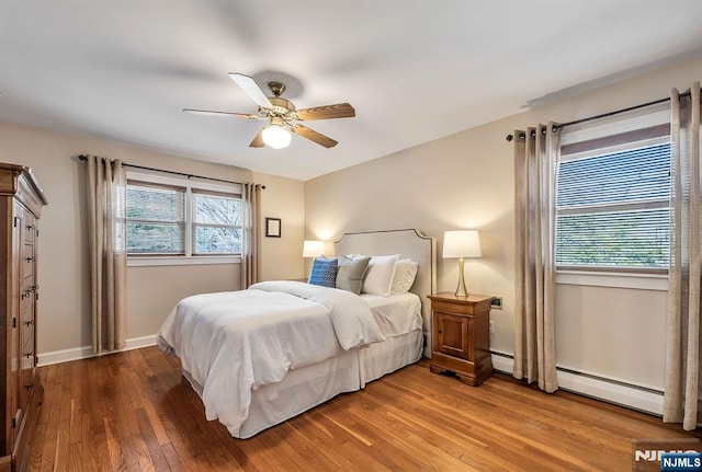 bedroom featuring ceiling fan, a baseboard heating unit, baseboards, and wood finished floors