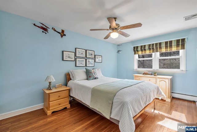 bedroom featuring wood finished floors, visible vents, baseboards, ceiling fan, and a baseboard heating unit