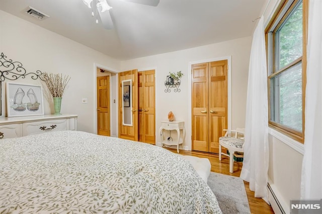 bedroom featuring a baseboard heating unit, light wood-type flooring, visible vents, and a ceiling fan