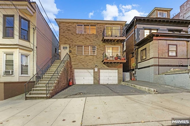 rear view of house featuring driveway, a garage, stairway, cooling unit, and brick siding