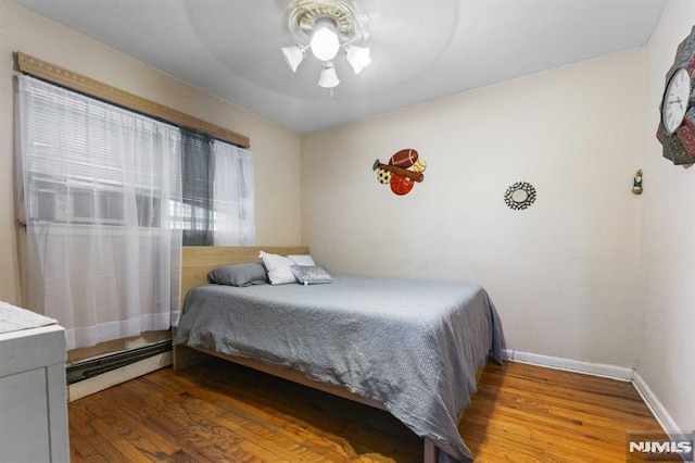 bedroom with baseboards, a baseboard heating unit, ceiling fan, and wood finished floors