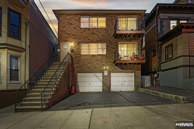 rear view of property with a balcony, a garage, brick siding, stairs, and driveway