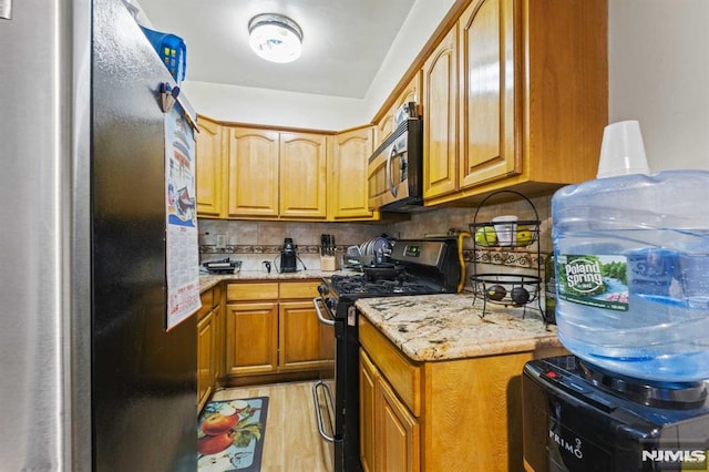 kitchen with light stone counters, stainless steel appliances, light wood-style floors, decorative backsplash, and brown cabinetry