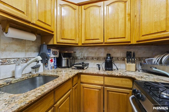 kitchen with light stone counters, brown cabinets, a sink, and decorative backsplash