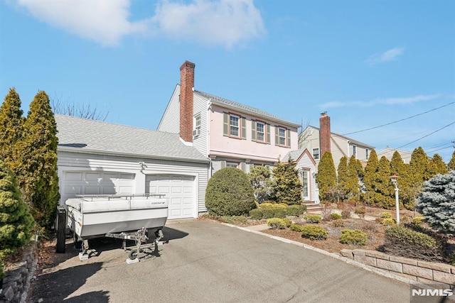 colonial-style house featuring a garage, driveway, a shingled roof, and a chimney