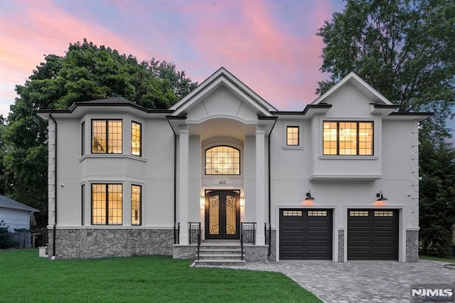 view of front of house featuring a garage, decorative driveway, french doors, a front lawn, and stucco siding