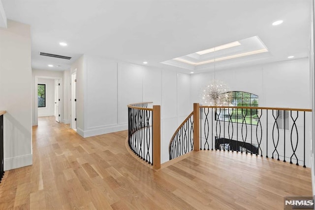 hallway with a chandelier, wood finished floors, visible vents, an upstairs landing, and a tray ceiling