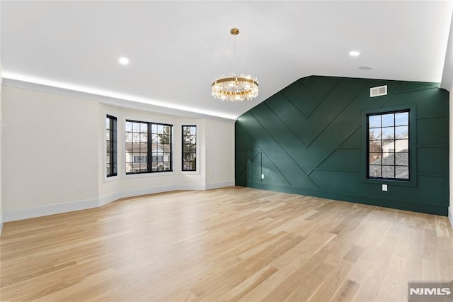 spare room with visible vents, baseboards, lofted ceiling, light wood-type flooring, and a chandelier