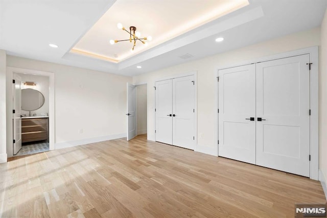 unfurnished bedroom with light wood finished floors, baseboards, an inviting chandelier, a tray ceiling, and two closets